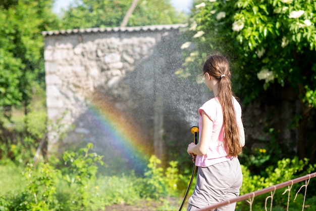 12-jarig meisje geeft planten water uit een tuinslang in de zon een regenboog is zichtbaar