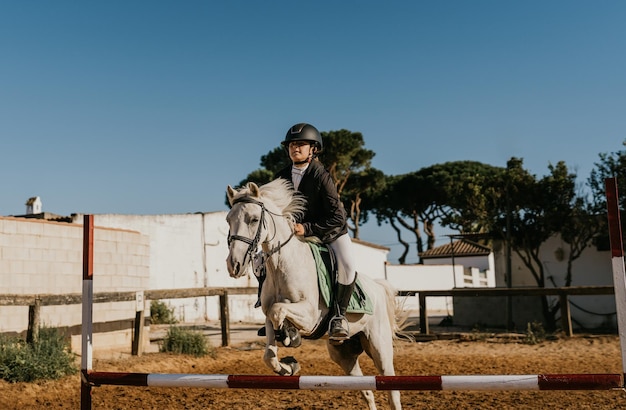 12-jarig meisje rijdt op een witte pony en springt over een hindernis bij een manege