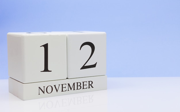 12 november. Dag 12 van de maand, dagelijkse kalender op witte tafel met reflectie, met lichtblauwe achtergrond