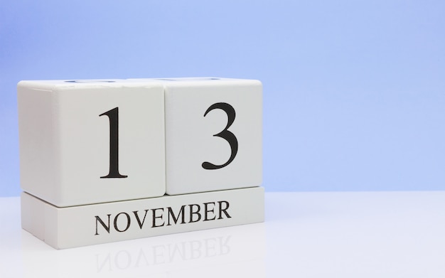 13 november. Dag 13 van de maand, dagelijkse kalender op witte tafel met reflectie, met lichtblauwe achtergrond