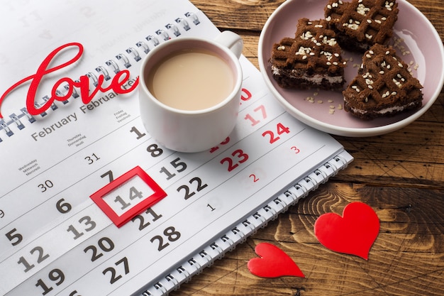 14 februari Kalender. Valentijnsdag concept, rode harten, het woord liefde en een kopje koffie.