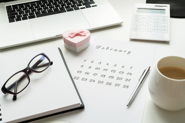 Calendario del 14 febbraio sullo spazio di lavoro con carta di san valentino cuore regalo rosa, tazza di caffè.