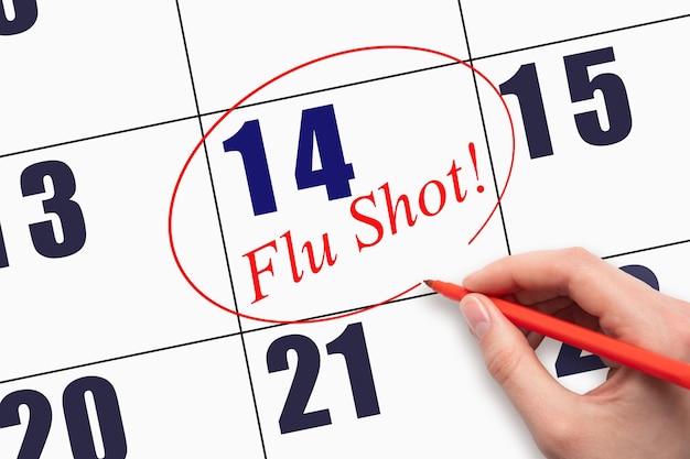 14th day of the month Hand writing text FLU SHOT and circling the calendar date
