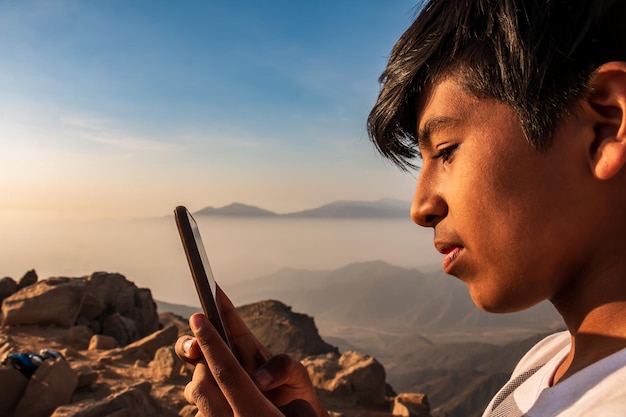 山からテキストメッセージを送信しようとしている手に携帯電話を持つ14歳の少年