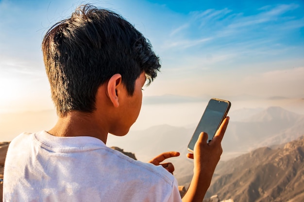 14yearold boy with cell phone in hand trying to send text message from a mountain