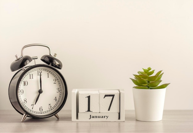 17 januari op een houten kalender, naast een retro wekker en een succulent in een minipot op een lichttafel.een dag in januari.winterdag.een kopie van de ruimte.werkplek.