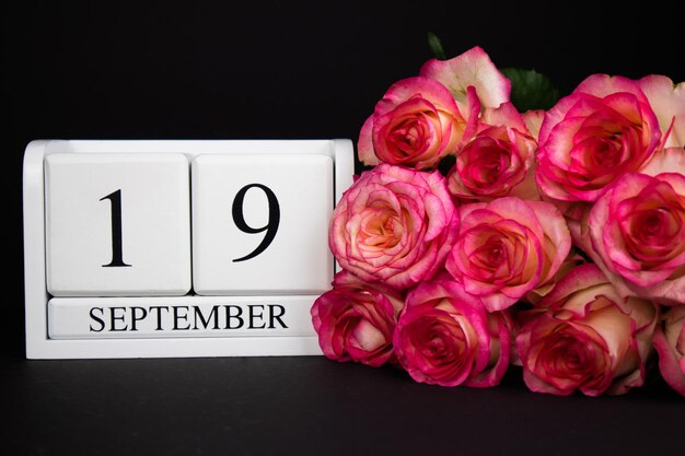 Foto 19 september houten kalender wit op een zwarte achtergrond roze rozen liggen in de buurt. briefkaart, plant, termijn