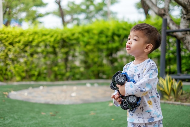 1歳のアジアの男の子が庭でおもちゃの車を持っています