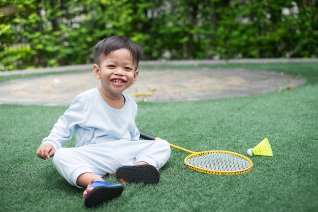 家でバドミントンをしながら座っている青い服を着た1歳のアジアの男の子