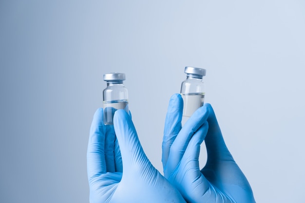 2 doses of vaccine. close-up. woman in blue medical gloves holding medication.