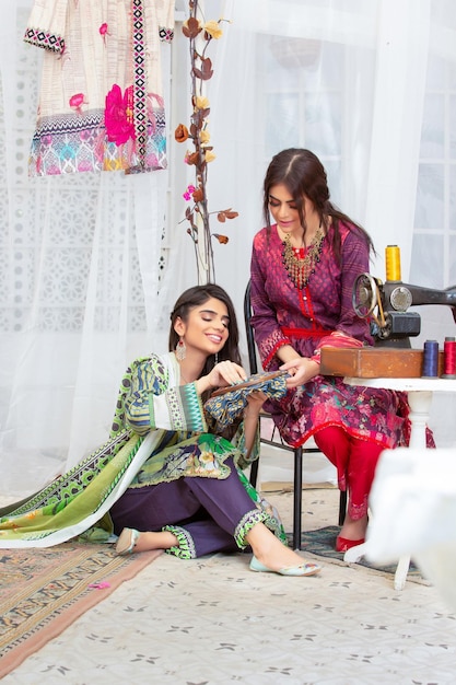 2 Smiling Girls Posing Together with Old Sewing Machine Wearing Floral Desi Dress for Fashion Shoot