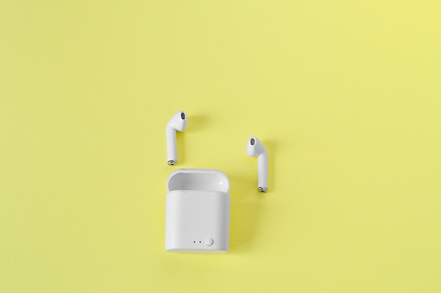 2 white wireless earphones in-ear with bluetooth on an yellow wall.copy space. Flat lay.