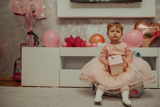 2 year baby girl in pink dress with her first birthday cake\
happy birthday carda cute little girl celebrates her first birthday\
surrounded by gifts