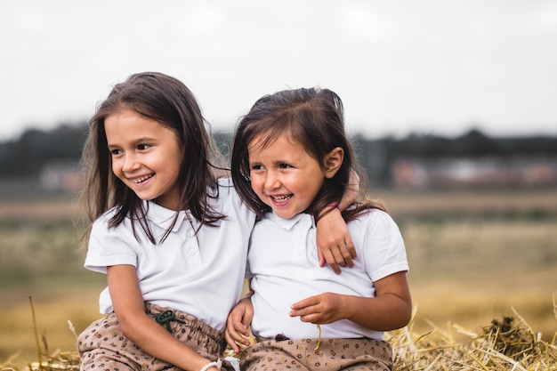 Foto ragazza di 2 anni che si siede sulla balla di fieno nel campo al tramonto