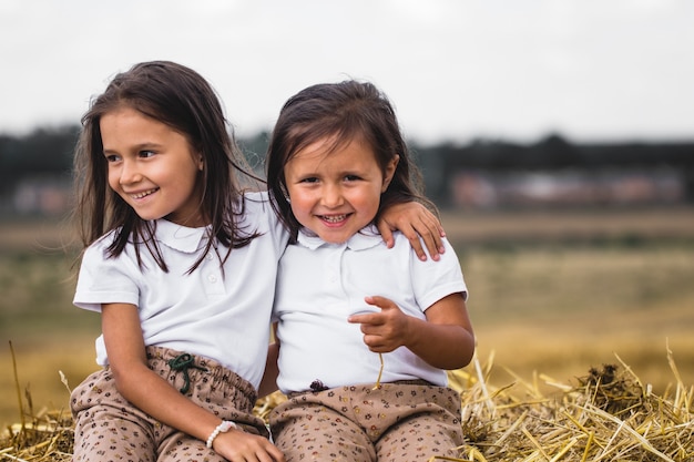 2 year old girl sitting on bale of hay in the field at sunset