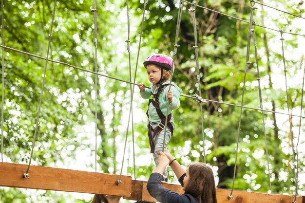 ヘルメットをかぶった2歳の少女と、アドベンチャーロープパークの安全装置。夏のレジャー