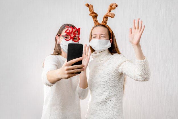 オンラインビデオ通話をしている2人の若い女の子またはサンタの帽子とフェイスマスクを持つ若い女性。検疫