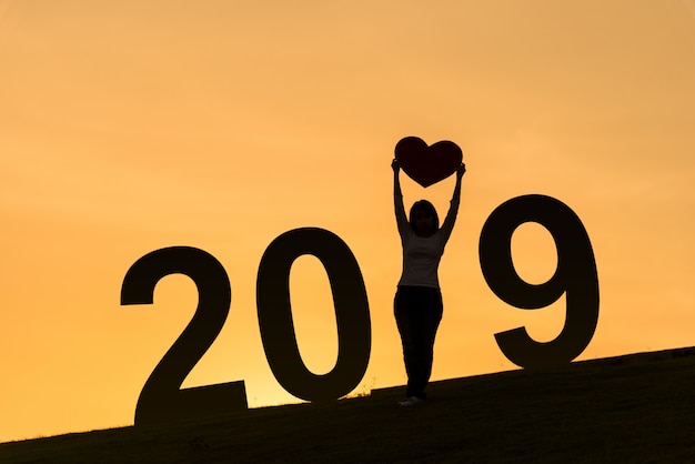 Foto una siluetta di 2019 nuovi anni di signora asiatica che sta sulla collina e che tiene cuore