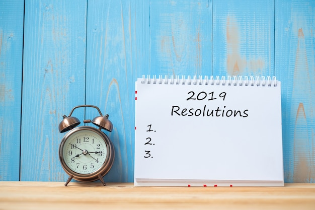 2019 resolutions text on notebook and retro alarm clock on table