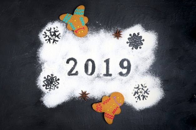 2019 text made with flour with decorations on black background with gingerbread Christmas 
