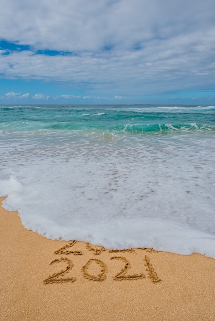 2020 2021 geschreven in het zand met een golf die 2020 wegspoelt