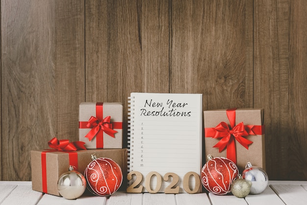 2020 houten tekst met kerstversieringen en nieuwjaarsresolutielijst geschreven op notebook over houten achtergrond