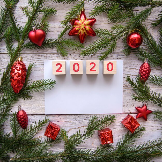 2020 in een kader van kerstboomtakken en rood speelgoed op een houten achtergrond