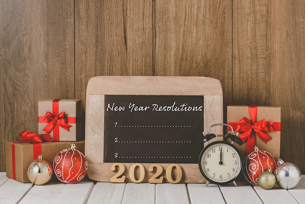 2020 wooden text and Alarm clock with Christmas ornaments and New Year's Resolutions List written on chalkboard 