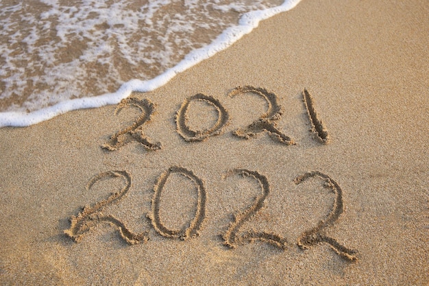 Foto 2021, 2022 anni scritti sul mare della spiaggia sabbiosa. l'onda spazza via il 2021.