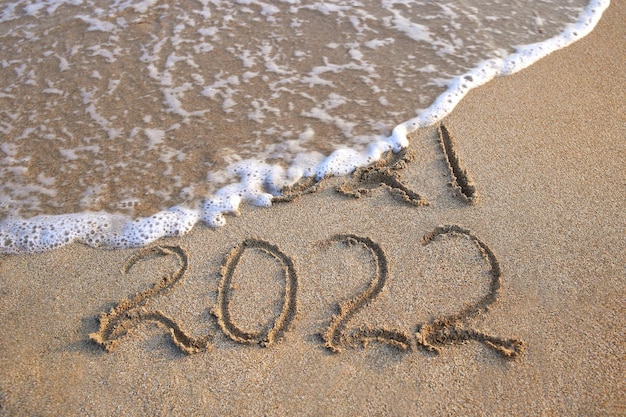 2021, 2022 years written on sandy beach sea. Wave washes away 2021.