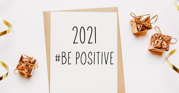 2021 год - позитивная нота с конвертом, подарками и золотой лентой на белом фоне. с рождеством и новым годом концепция