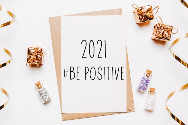 2021 be positive note with envelope, gifts and gold glitter stars on white surface. merry christmas and new year concept
