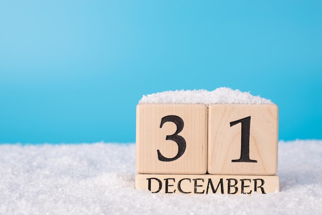 Photo 2021 coming soon concept. close up photo of wooden cube calendar showing the last day of old year isolated on blue background with snow