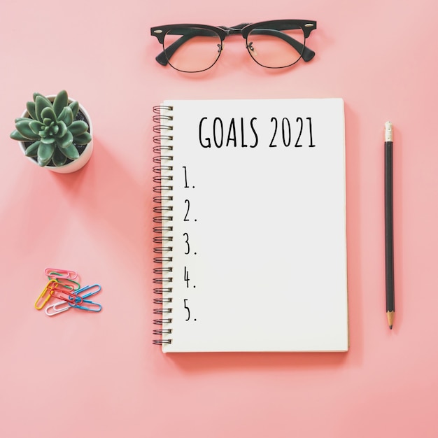 2021 New year concept. Goals list in notepad, smartphone, stationery on pink pastel color with copy space