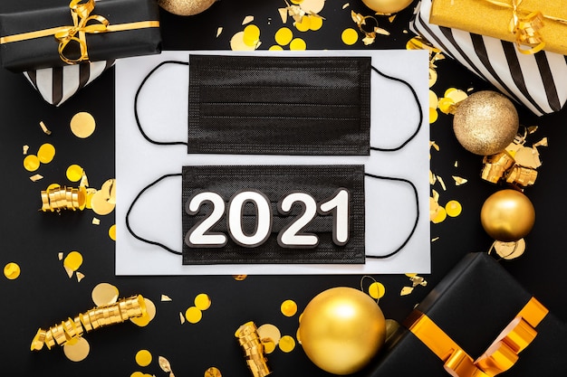 黒の医療用フェイスマスク、金のお祝いの装飾が施された2021年のテキストレタリング。新年のcovid19。