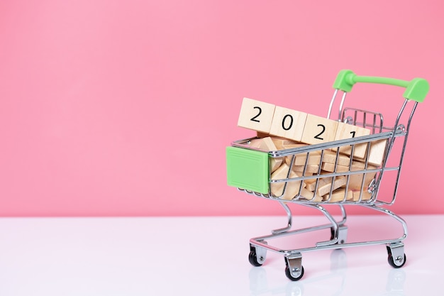 2021 with wood cube in shopping cart on pink background. Happy new year concept.