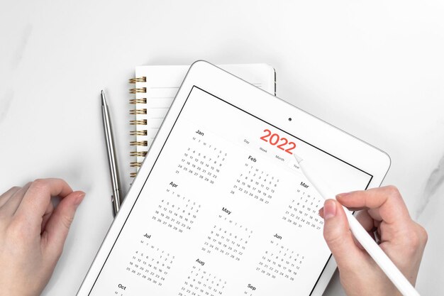 2022年のカレンダーのクローズアップ、タブレットコンピューターの画面。白い大理石の背景。予定と会議の計画の概念