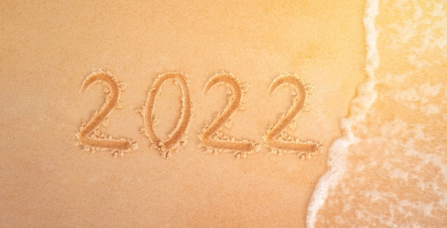 2022 figures on sandy beach in the background New Year's Eve. sea wave washes away inscription 2022 on the yellow sand close-up. New year holidays on the beach.