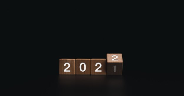 2022 Happy New year welcome and Merry Christmas banner. Flipping wooden cube blocks for changing the year from 2021 to 2022 on dark background.