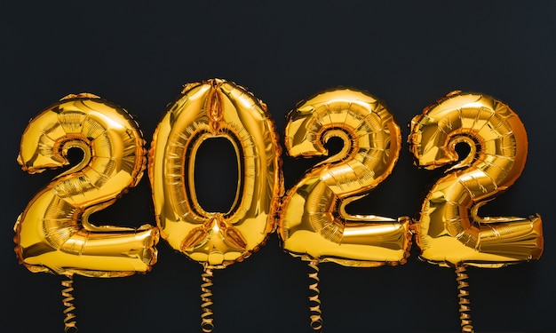 2022 jaar ballon gouden tekst op zwarte achtergrond met gouden feestelijk decor. Gelukkig nieuwjaarsuitnodiging met kerst goudfolie ballonnen 2022 cadeaubon.