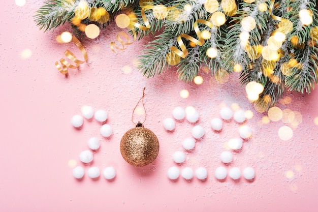 2022 made from snowballs and Christmas ball on pink background, spruce branches and golden bokeh lights.