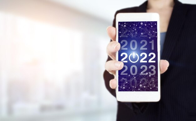 2022 new year. Hand hold white smartphone with digital hologram 2022 sign on light blurred background. Welcome year 2022. Business new year card concept