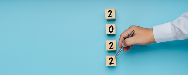 2022 new year number on wood block with hand pointing to plan with copy space of blue background banner