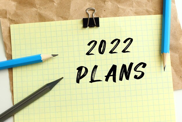 구겨진 크라프트지 위에 노란색 종이에 2022 PLANS 글자. 연필과 종이 클립.