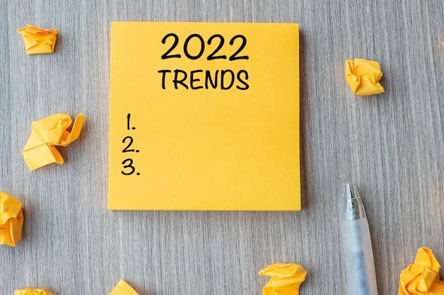 2022年トレンドワードペンと木製のテーブルの背景に砕いた紙で黄色のノートに。新年の新しいスタート、決議、戦略、目標のコンセプト