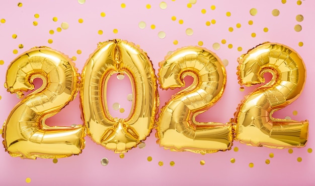 ピンク色の背景に紙吹雪と2022年の金の風船のテキスト新年あけましておめでとうございます2022レタリング