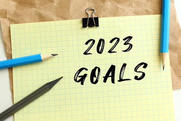 2023 GOALS lettering on a yellow sheet of paper over crumpled kraft paper Pencils and paper clip