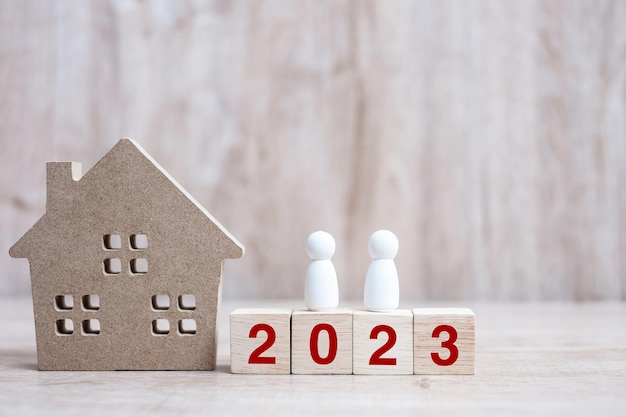 2023 Happy New Year with house model and people on wooden background Banking real estate investment financial savings and New Year Resolution concepts