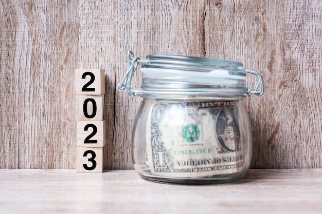 2023 Happy New Year with US dollar money glass American on wood table background business investment retirement planning finance Saving and New Year Resolution concepts