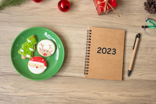 2023 notebook zwarte kerstkoekjes en pen op houten tafel Bovenaanzicht en kopieer ruimte Xmas Happy New Year doelen resolutie takenlijst strategie en plan concept